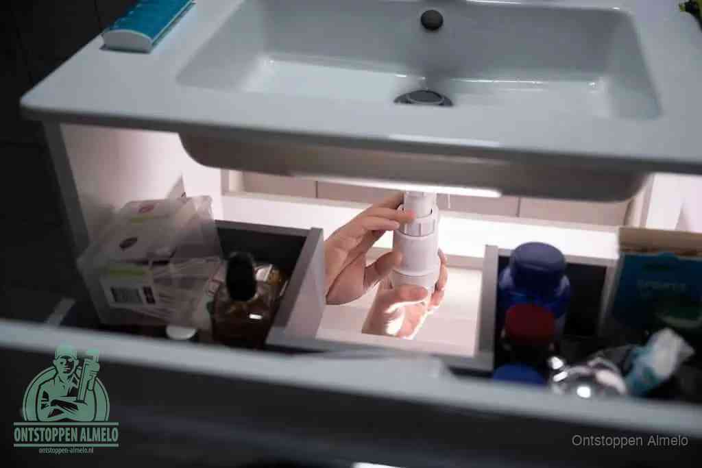 Een pompfles met zeep boven een wastafel, de heet water en afwasmiddel-methode om een vetprop in de afvoer los te maken in Almelo