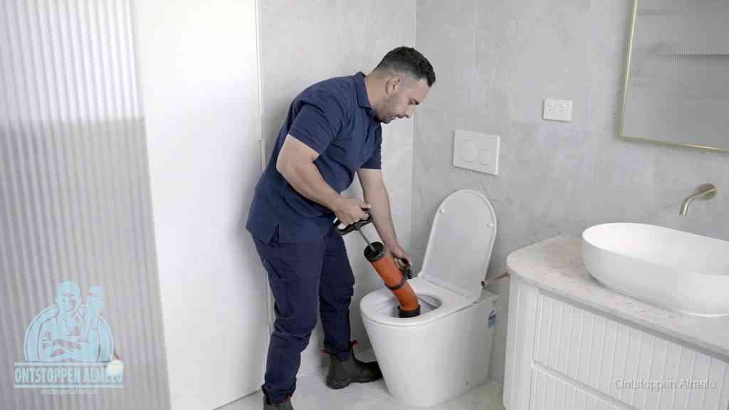 Een monteur buigt over een wandcloset en duwt met de hand een persluchtontstopper in de toiletpot om de verstopping handmatig los te maken in Almelo