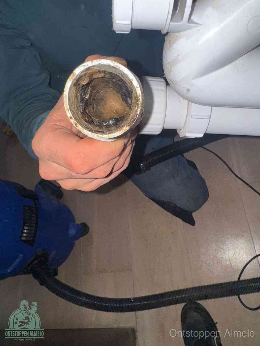 Een hand houdt een losgekoppeld PVC-afvoerbuisstuk vast dat van binnen volledig is dichtgeslibd met vet, vuil en aanslag, de meest voorkomende oorzaak van een verstopte afvoer in Almelo