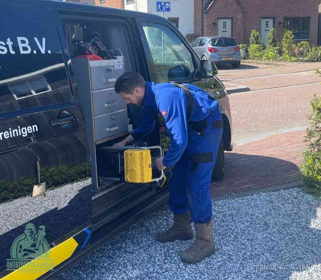 Een monteur pakt buiten op de oprit gereedschap uit de bedrijfsbus, het moment om een professional in te schakelen voor een verstopte afvoer in Almelo