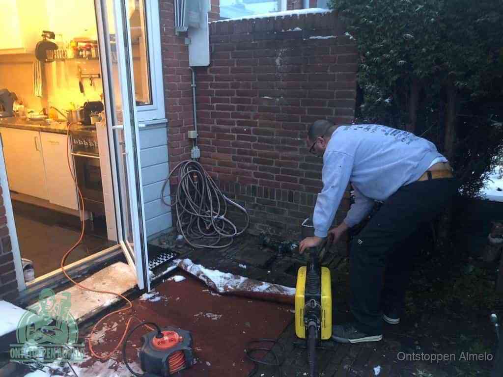 Een monteur werkt buiten bij een open riool-/grondput met een elektrische ontstoppingsmachine om een verborgen afvoerprobleem op te sporen in Almelo