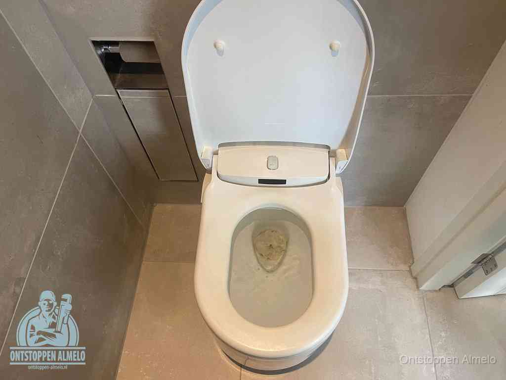 Een wit hangtoilet waarin een prop wc-papier op het water blijft drijven, een duidelijk signaal van een verstopte wc in Almelo