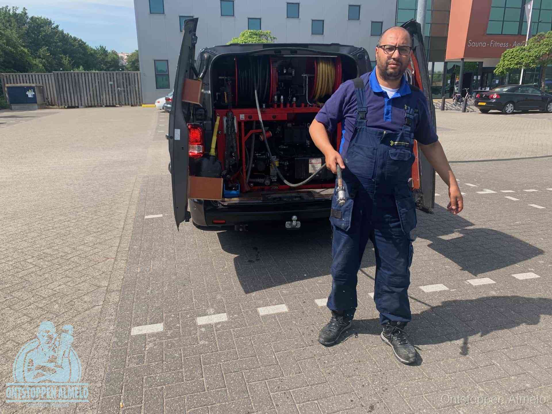 Een monteur bij zijn bestelbus met een hogedruk- en rioolreinigingsunit, klaar om de oorzaak van terugkerende wc-verstoppingen aan te pakken in Almelo