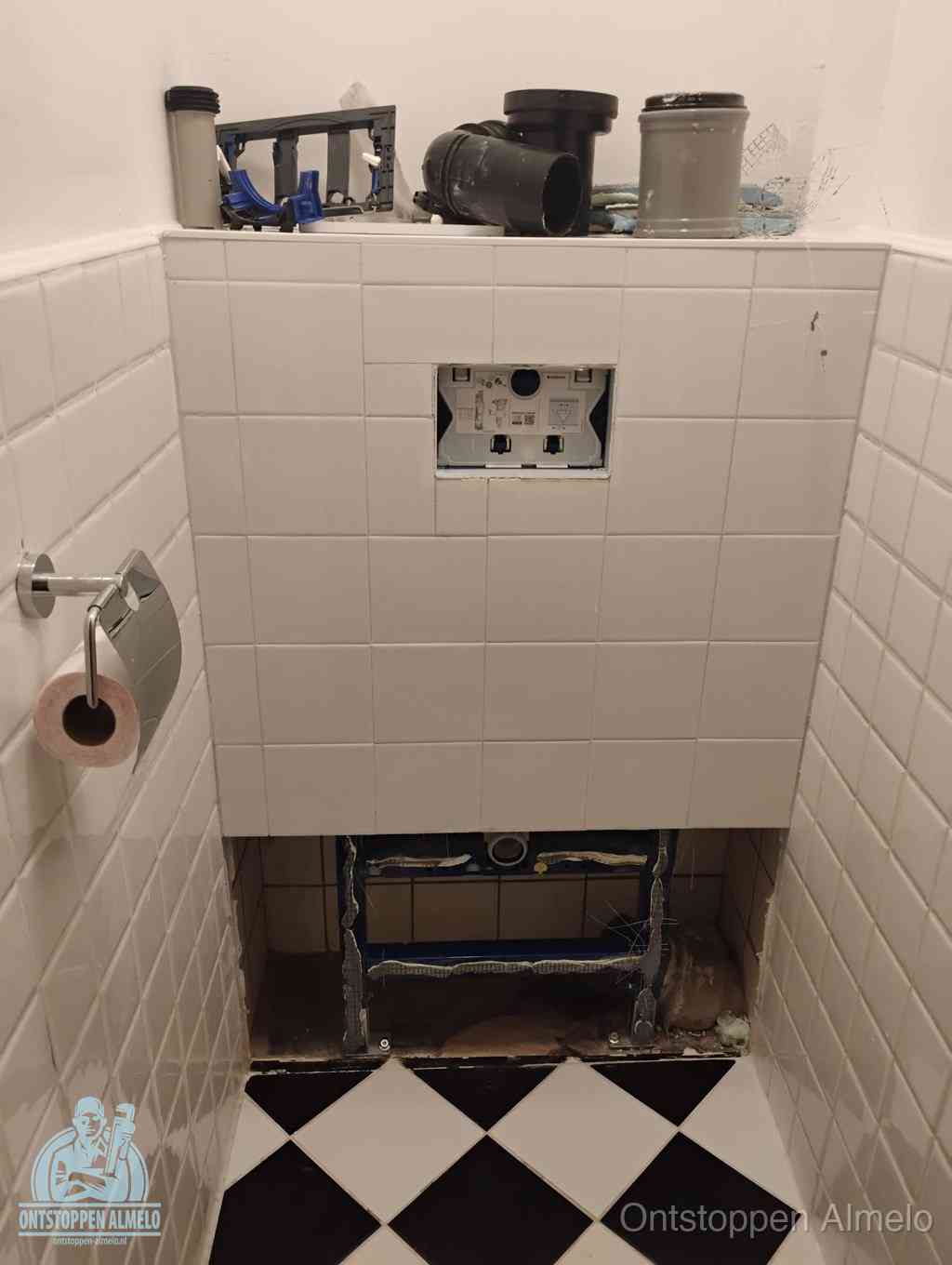 Een toiletruimte waar het hangtoilet en de inbouwreservoir-onderdelen zijn vrijgelegd voor onderhoud, periodiek nazicht voorkomt een wc-verstopping in Almelo