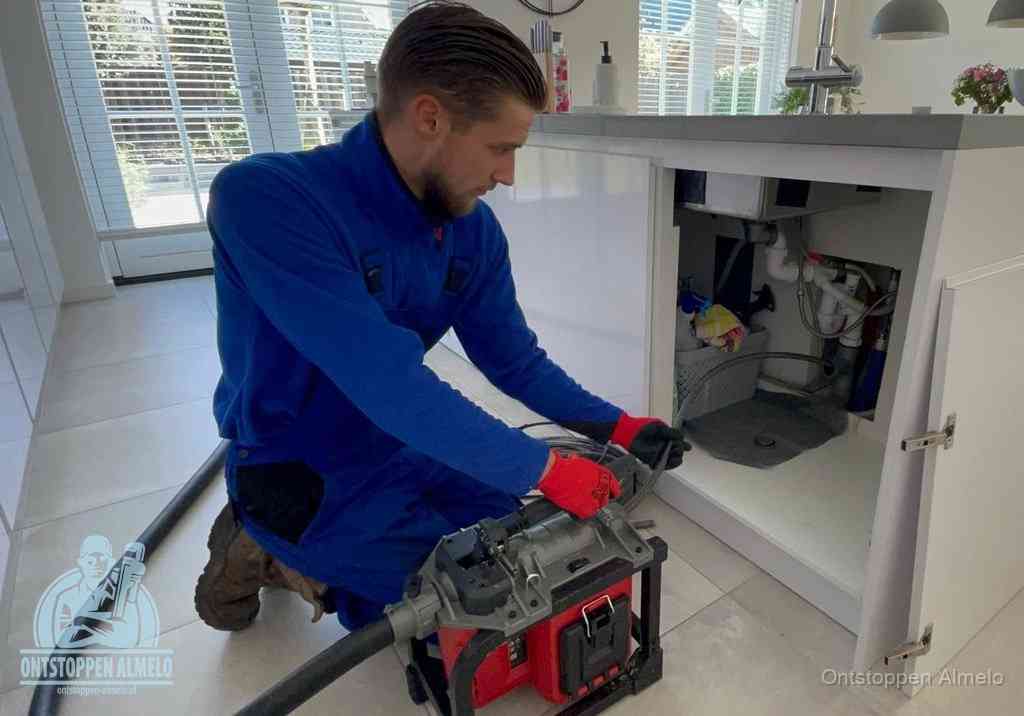Een monteur voert een professionele elektrische ontstoppingsmachine in de afvoer onder de spoelbak tijdens het gootsteen ontstoppen in Almelo