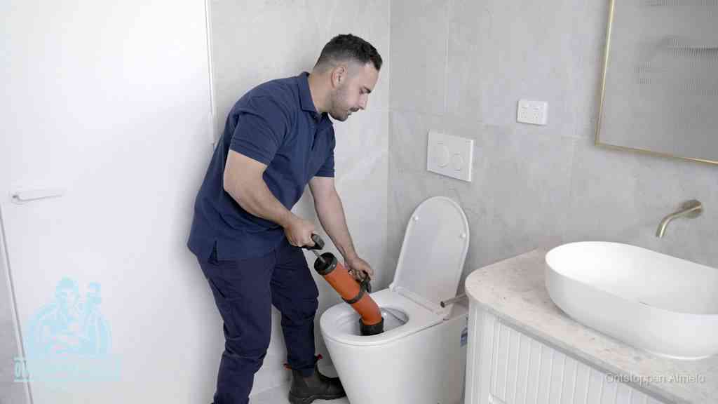 Een monteur gebruikt een handmatige perspomp (toiletontstopper) op een wandcloset tijdens het professioneel wc ontstoppen in Almelo