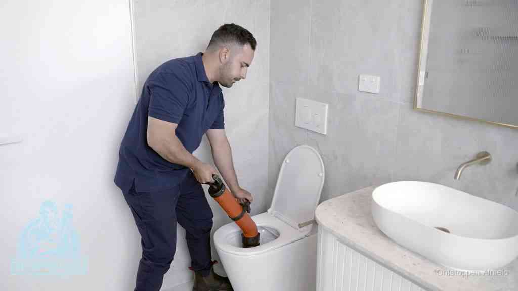 Een man gebruikt een handmatige luchtdruk-ontstopper in een modern betegeld toilet om zelf de wc te ontstoppen in Almelo